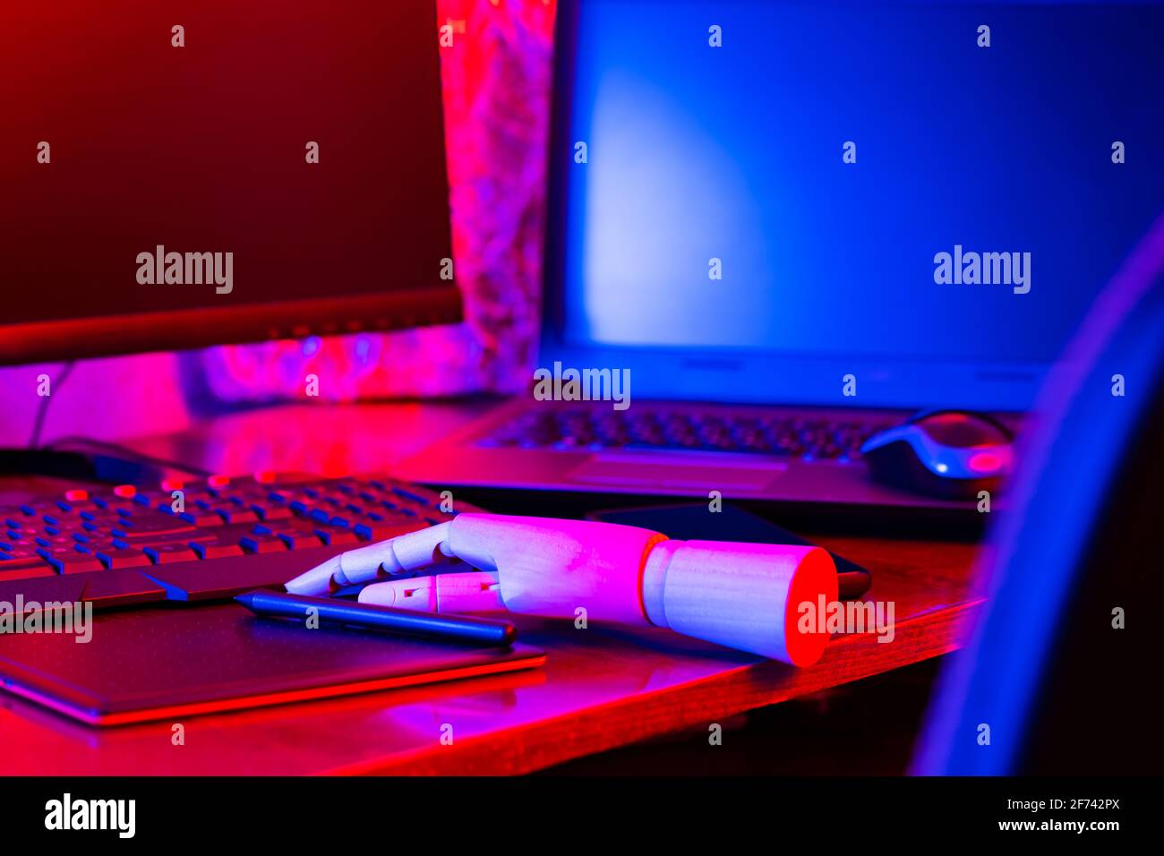 Digital design concept with a robot. Creative designer workplace in neon light. Digital tablet for drawing and an artificial arm with a pen. Distant w Stock Photo