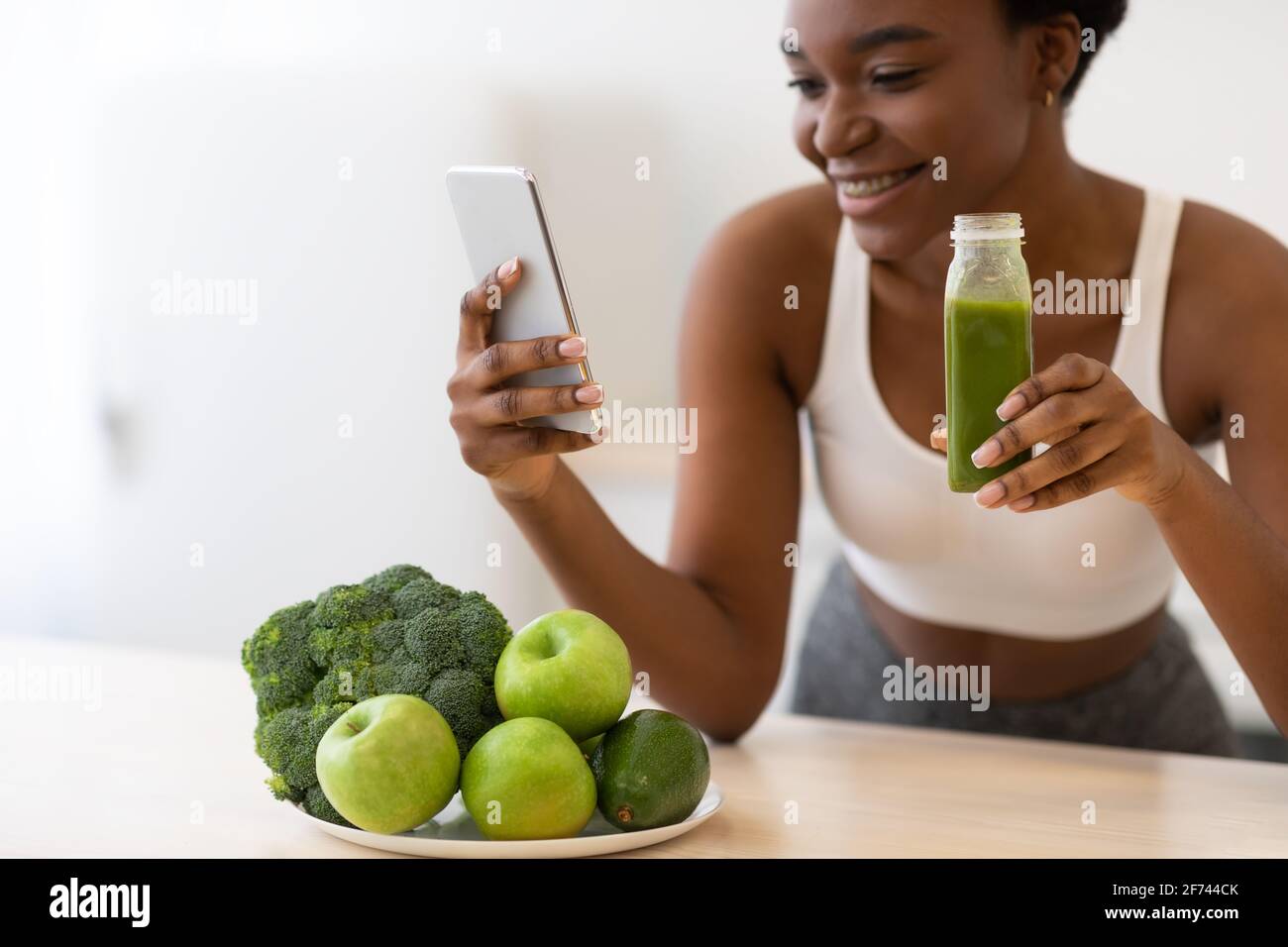 Black Fitness Woman Using Mobile Phone Drinking Smoothie In Kitchen Stock  Photo - Alamy