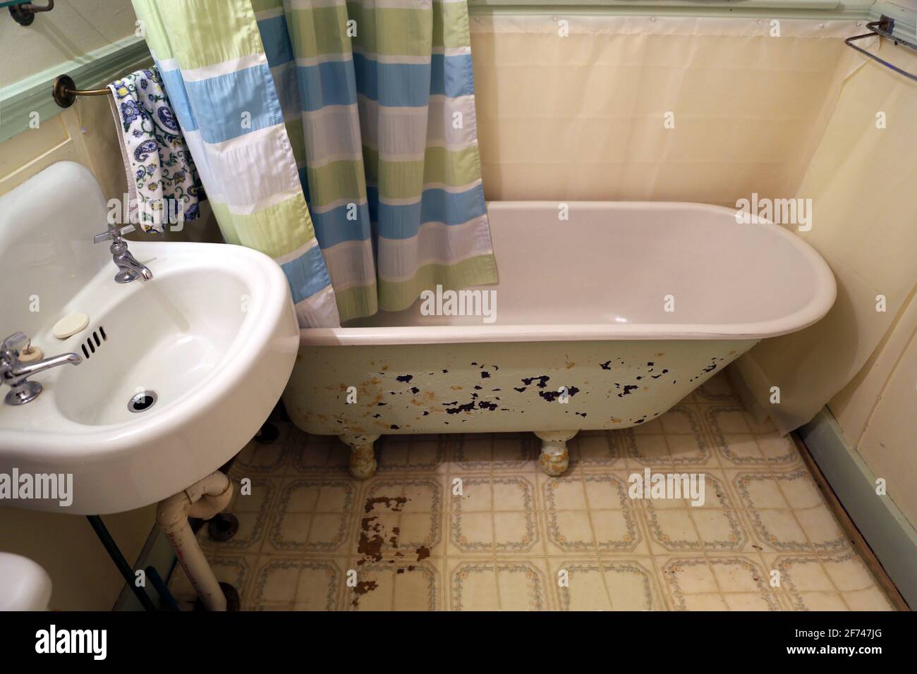 Old retro style home, trailer, cabin or cottage small outdated rustic bathroom with tile linoleum, and peeling paint on iron claw foot tub for remodel Stock Photo