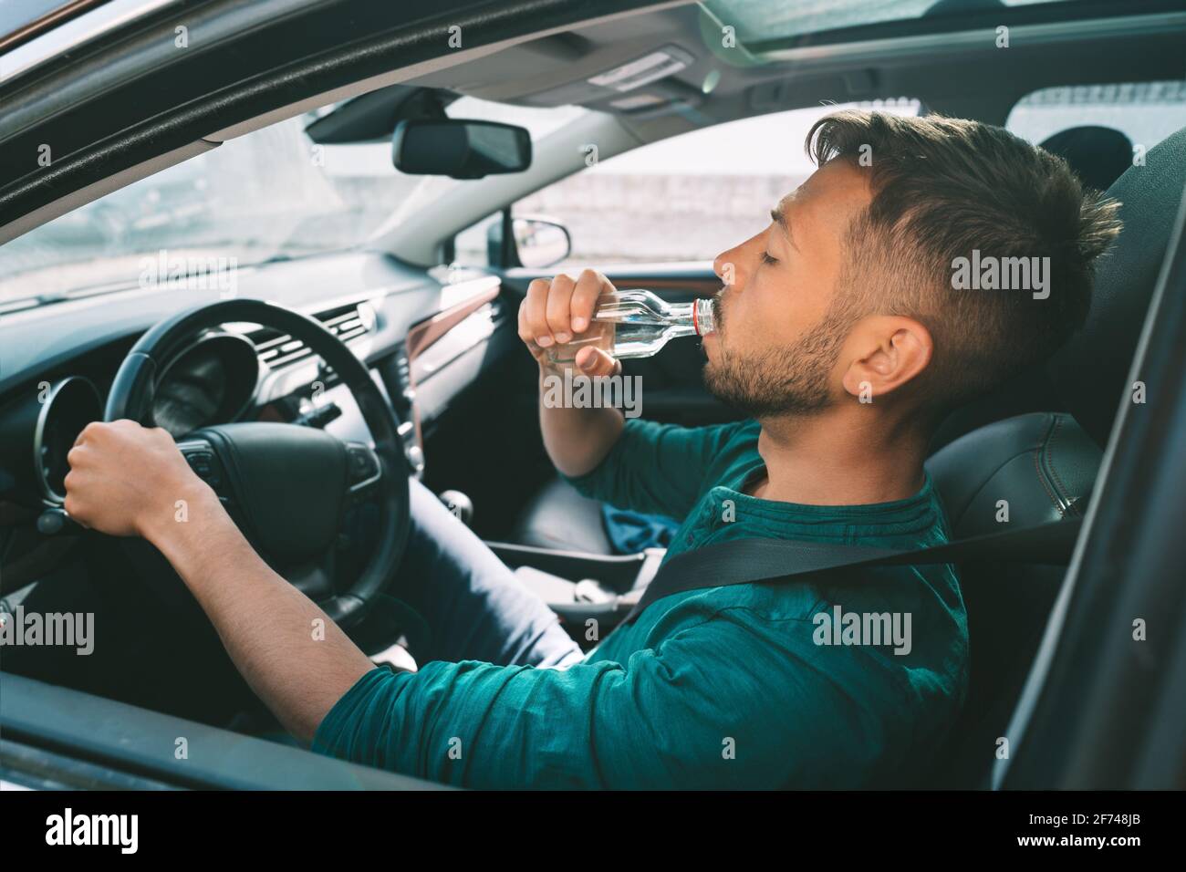 Driving under alcohol influence. Drunk driving. Young man drives a car with a bottle of vodka. Drunkenness. Dangerous driving concept Stock Photo
