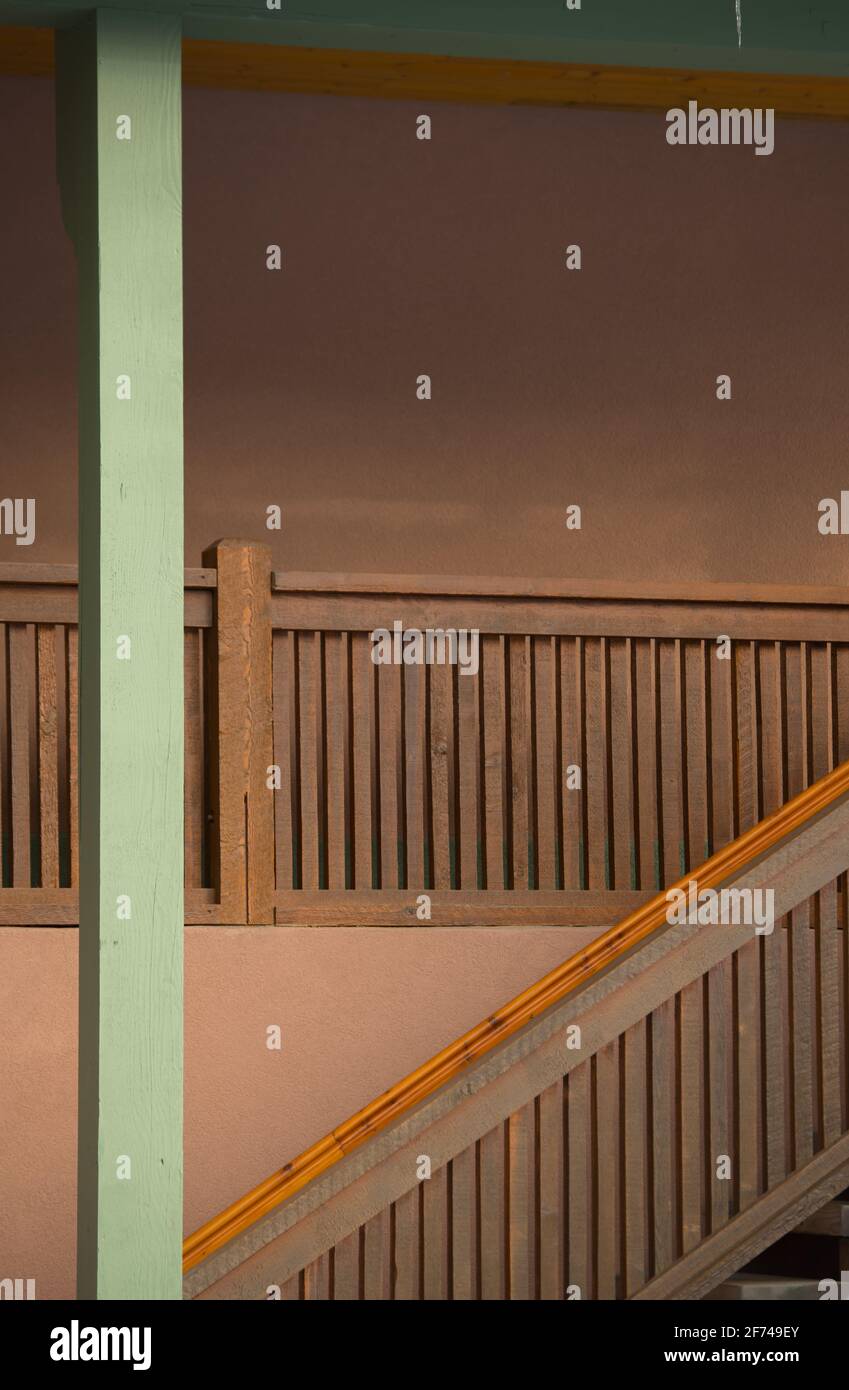 wooden stair case of exterior home or apartment against peach coloured exterior concrete wall and green painted upright support pole showing angles Stock Photo