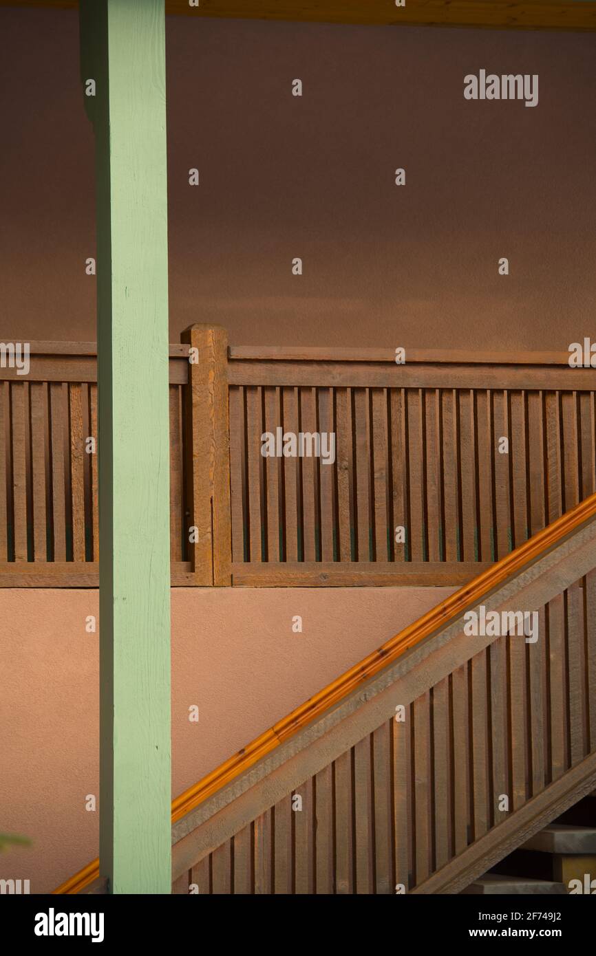 wooden stair case of exterior home or apartment against peach coloured exterior concrete wall and green painted upright support pole showing angles Stock Photo