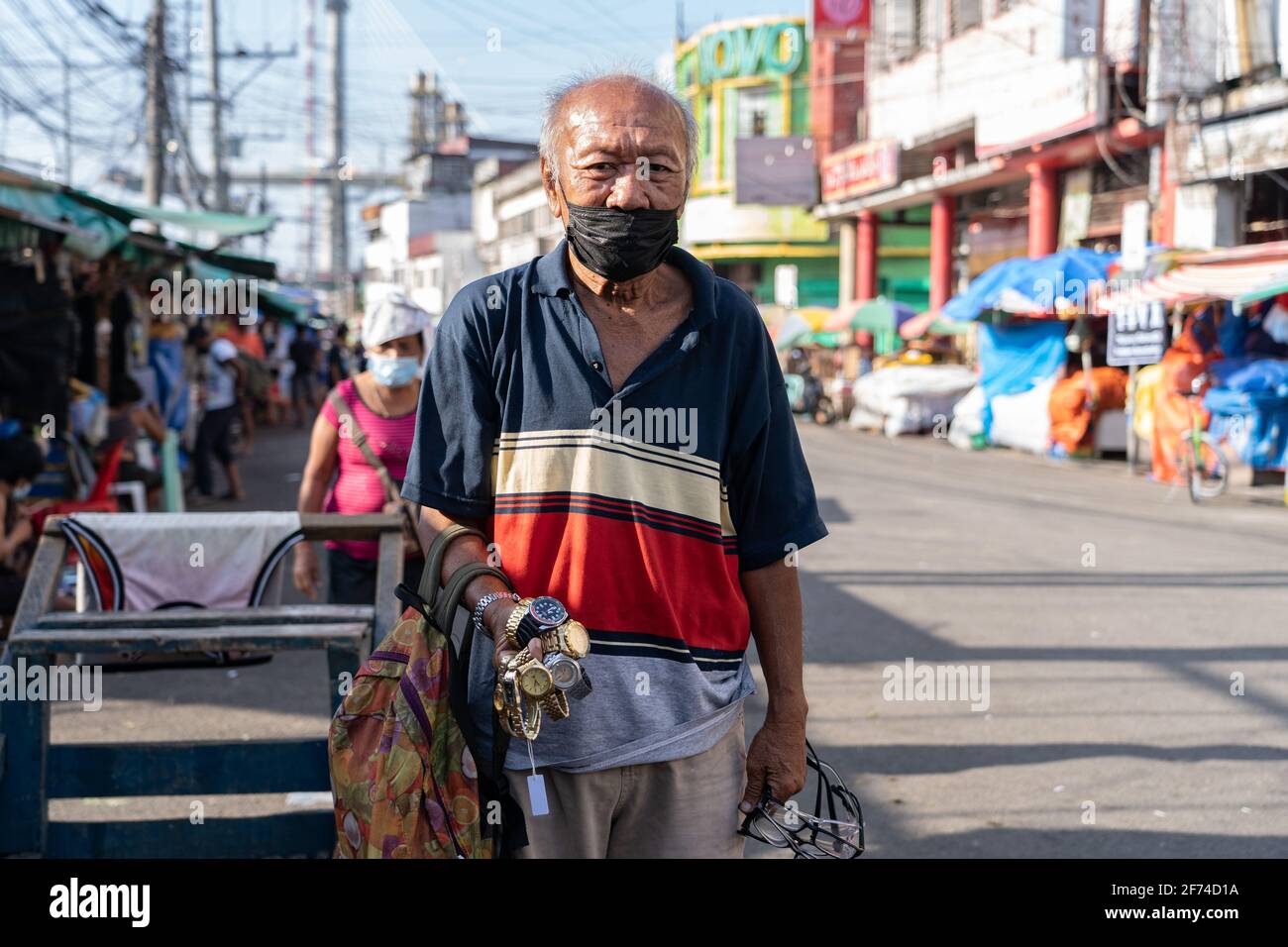 A man wearing a face mask during Covid-19, selling watches and face shields in a poor area of Cebu City, Philippines Stock Photo