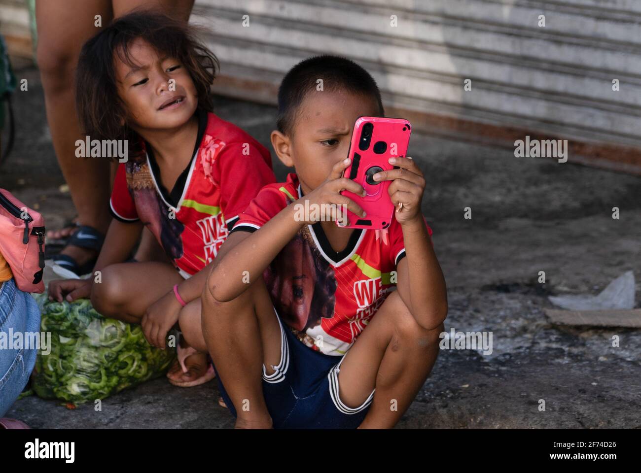 A young child in a poor area of Cebu City, Philippines using a mobile phone whilst a young girl looks on Stock Photo