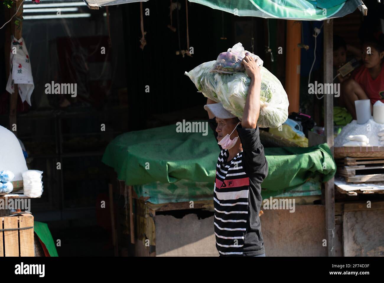 A man carrying a heavy load of vegaetables in a market area, Cebu City, Philippines Stock Photo