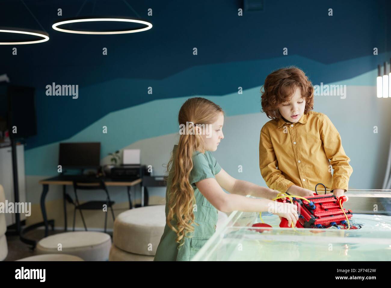 Portrait of two kids putting robo boat in water while experimenting with technology at robotics lab in school, copy space Stock Photo