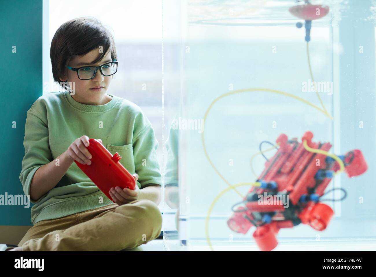 Portrait of smart boy operating robotic boat in water tank while experimenting in engineering lab at school, copy space Stock Photo