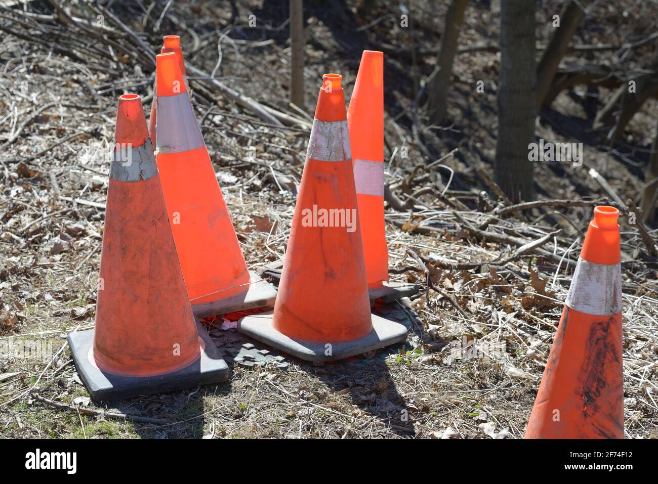 neon orange and reflective white traffic cones, pylons, road cones, or construction cones sitting on the ground off by the side of a roadway Stock Photo