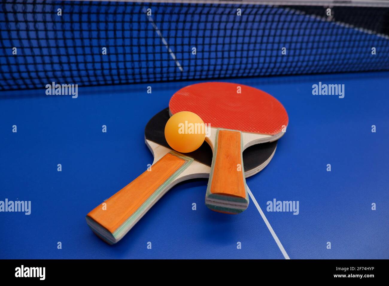 on the tennis table is a ball and two table tennis rackets Stock Photo