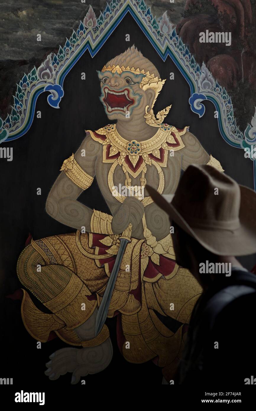 A visitor paying attention to a mural painting on an entrance wall, part of a gallery of mural paintings depicting Ramakien (Thai version of Ramayana epic) which is located at the Wat Phra Kaew (Temple of Emerald Buddha), inside Grand Palace complex in Bangkok, Thailand. Thailand is the first Southeast Asian country to reduce quarantine restrictions--from 14 days to 10 days--to speed up the recovery of its tourism sector, according to South China Morning Post on April 2, 2021. The decision was made to speed up the recovery process, that was previously forecasted to be 'a slow return.' Stock Photo