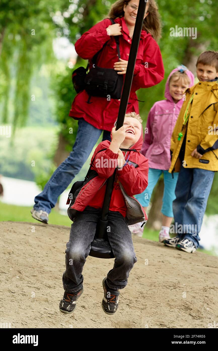 Boy having fun swinging on a large swing in a park with mother and ...
