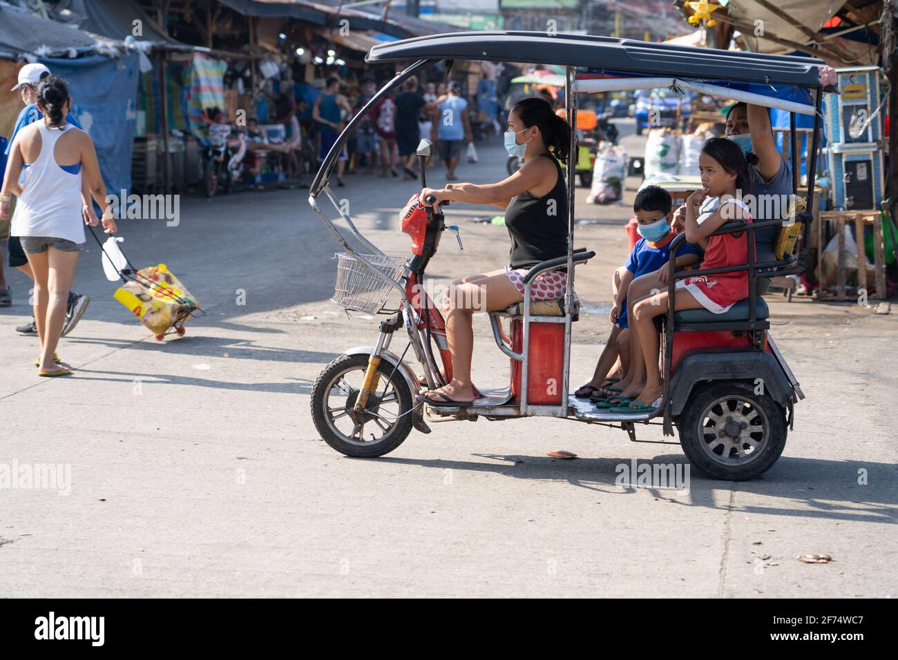 A woman driving a three wheeled  electric vehicle within a market area, Cebu City, Philippines Stock Photo