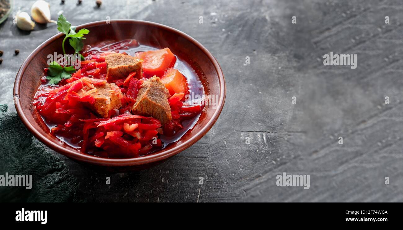 Red borsch with vegetables and meat in a clay plate. Steam from hot tomato soup. Dark background. Delicious healthy lunch. Copy space Stock Photo