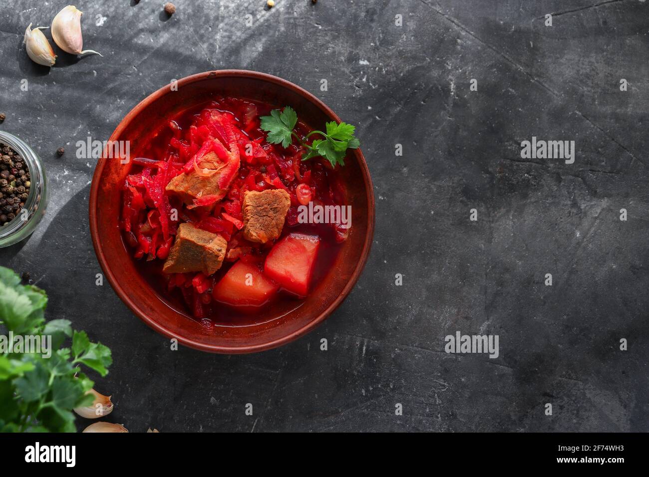 Red borsch with vegetables and meat in a clay plate. Steam from hot tomato soup. Dark background. Delicious healthy lunch. Top view. Copyspace Stock Photo