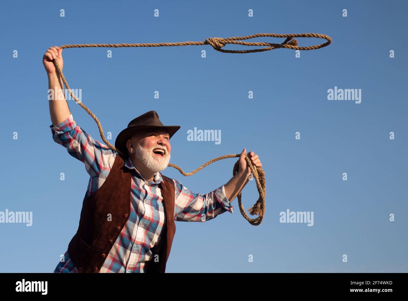 Old cowboy with lasso rope at ranch or rodeo. Bearded western man with  brown jacket and hat catching horse or cow Stock Photo - Alamy