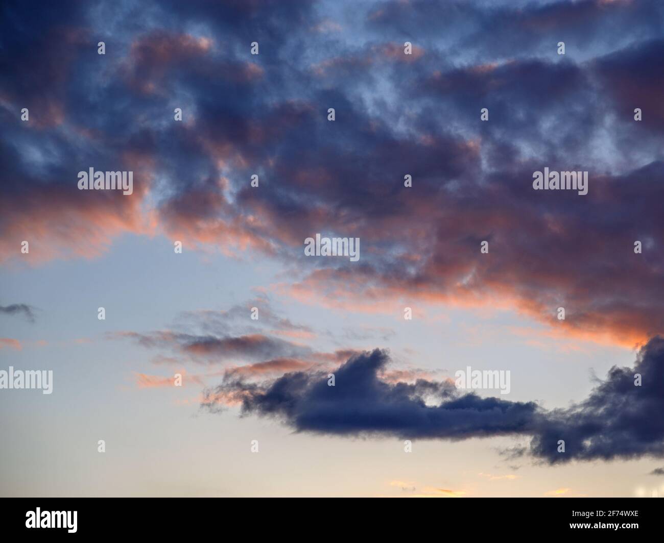 Dark clouds are illuminated by setting sun in spring sky. Stock Photo