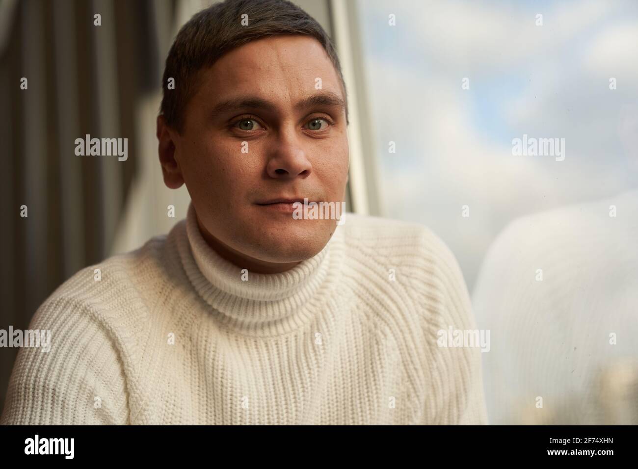 The handsome man in the room smiles and looks at camera. A man in a white sweater. Copy space. High quality photo Stock Photo