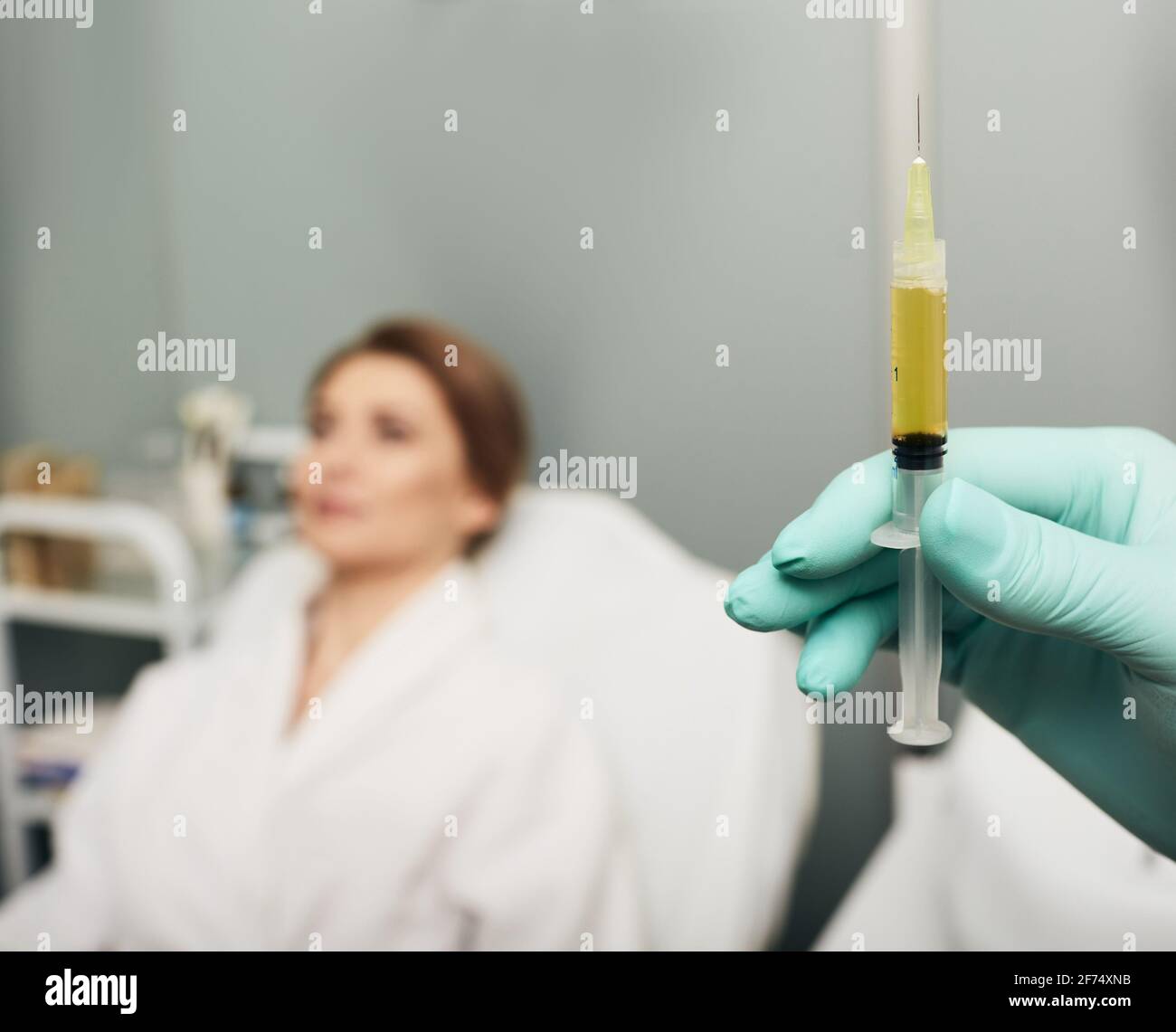 Syringe with a patient's blood plasma in a cosmetologist's hand for a plasmolifting of a woman's skin. Plasma therapy, skin cell restoration Stock Photo