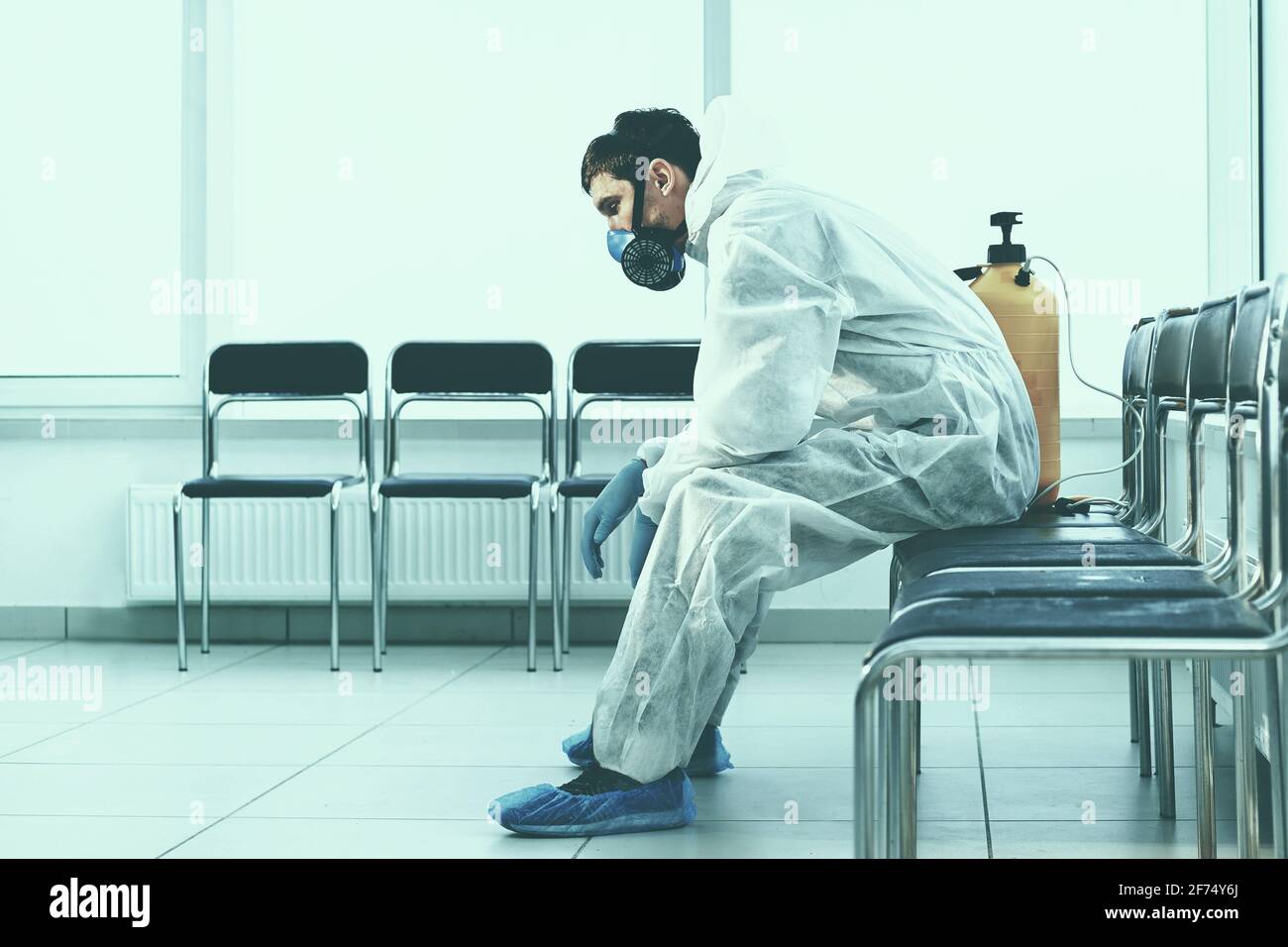 tired medical orderly in a protective suit sitting in a public waiting room. Stock Photo