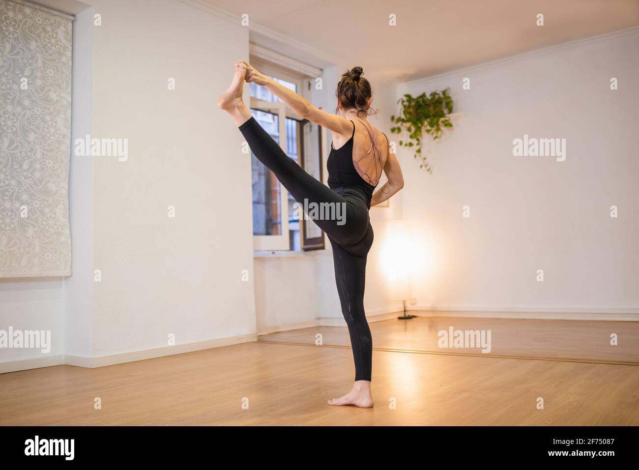 Side view of anonymous flexible barefoot female performing Extended Standing Hand to Toe pose on floor against luminous lamp Stock Photo