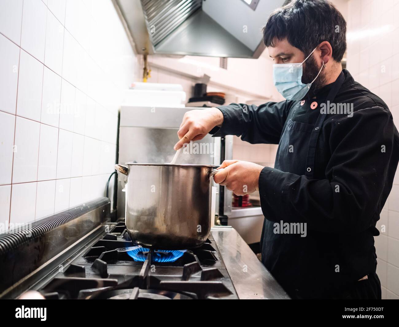 https://c8.alamy.com/comp/2F750DT/side-view-of-professional-male-cook-in-mask-stirring-dish-in-saucepan-while-cooking-on-stove-in-kitchen-of-restaurant-2F750DT.jpg