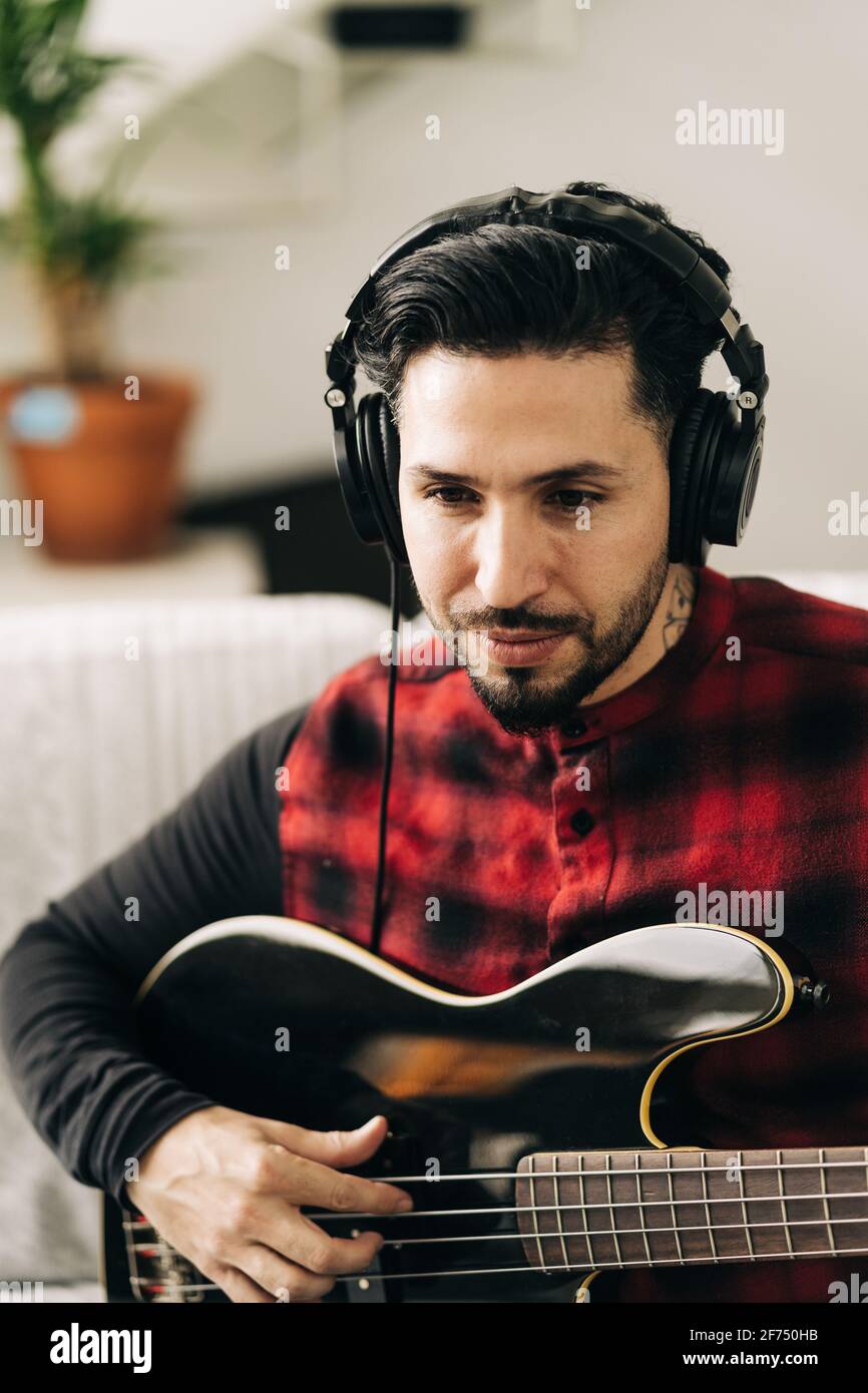 Adult male musician in headphones playing bass guitar against netbook