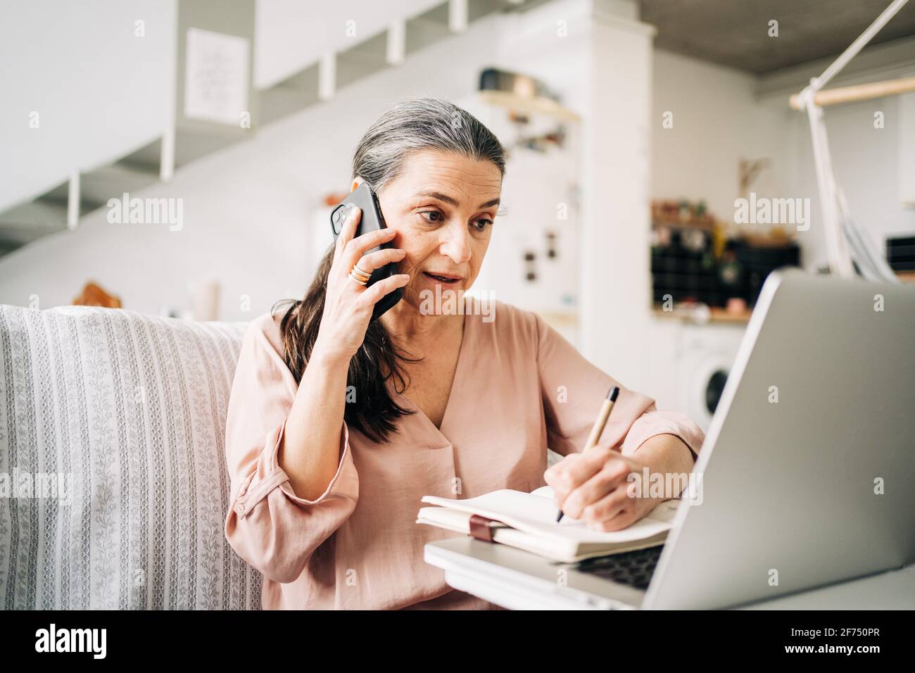 Concentrated middle aged female having phone call and taking notes in ...