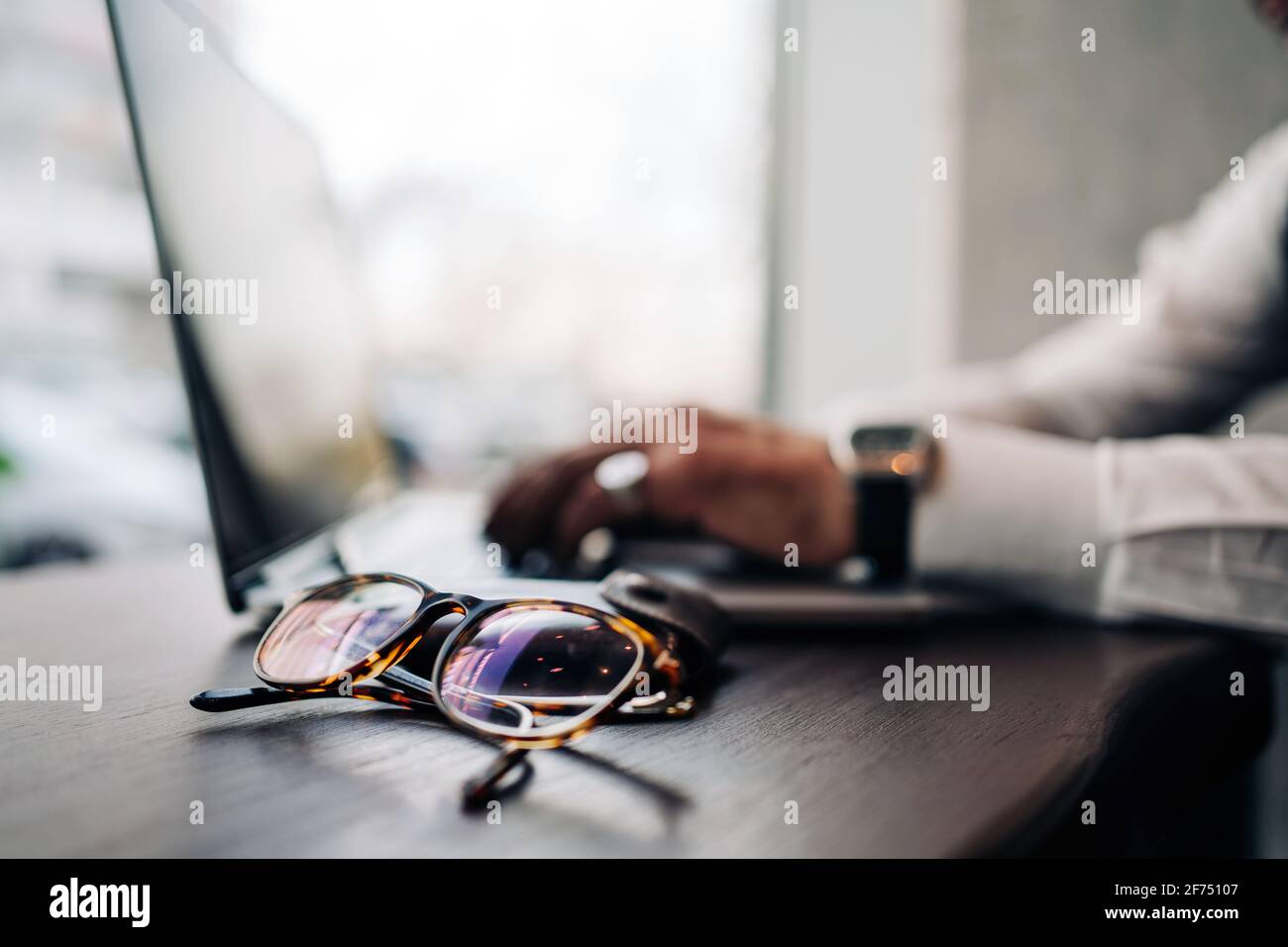 Crop anonymous male executive using portable computer at table with modern eyeglasses in cafe Stock Photo
