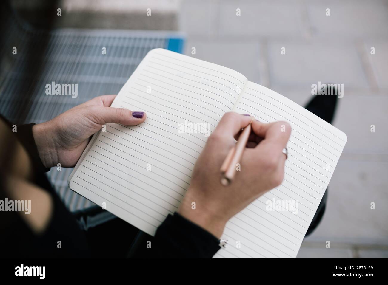High angle of crop unrecognizable female entrepreneur sitting on bench in city and writing business plan in notebook Stock Photo