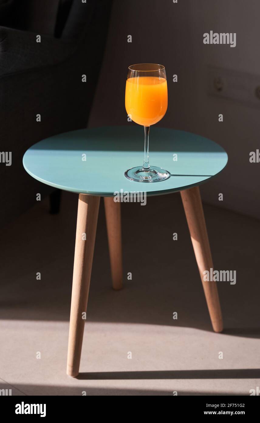 From above of glass of fresh orange juice placed on small round table near comfortable sofa in sunlight Stock Photo