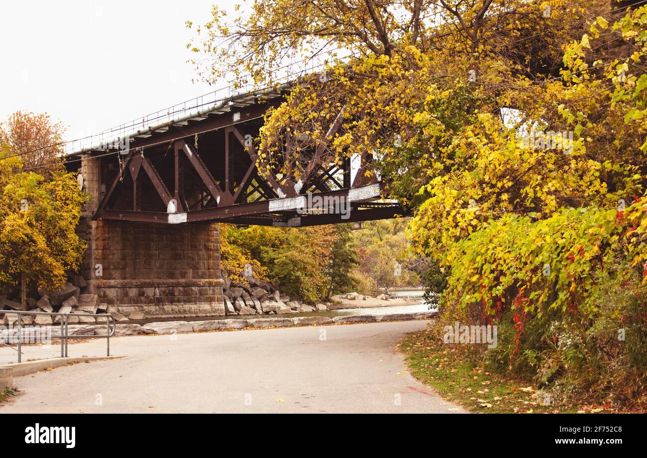 A bridge surrounded by autumn foliage over a river in Toronto, Ontario under an overcast sky. Stock Photo