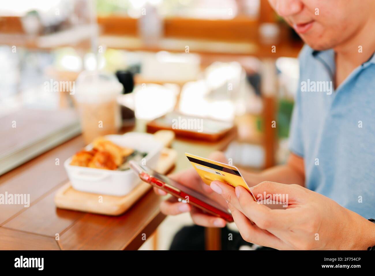 Closeup of hands of handsome young Asian man making card payment using smartphone while eating lunch in modern cafe with social distancing norms due to coronavirus Stock Photo