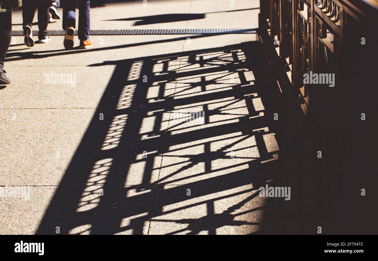 A busy sidewalk in Chicago covered in shadowed patterns from the railing beside it. Stock Photo
