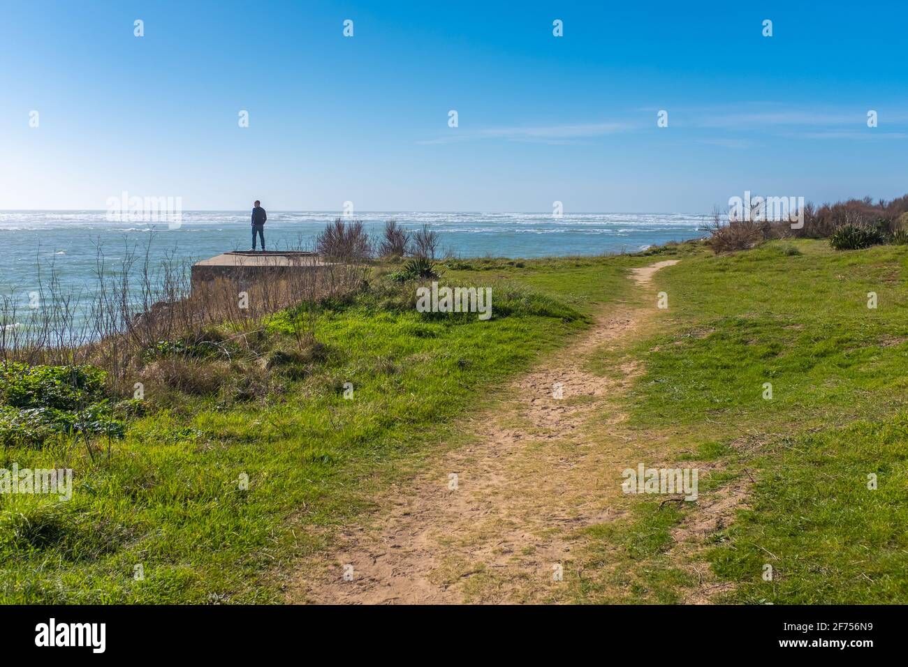 Ars-en-Ré, France - February 24, 2020: Man seen from afar, looking at the sea on top of a blockhaus, on a sunny late winter day Stock Photo