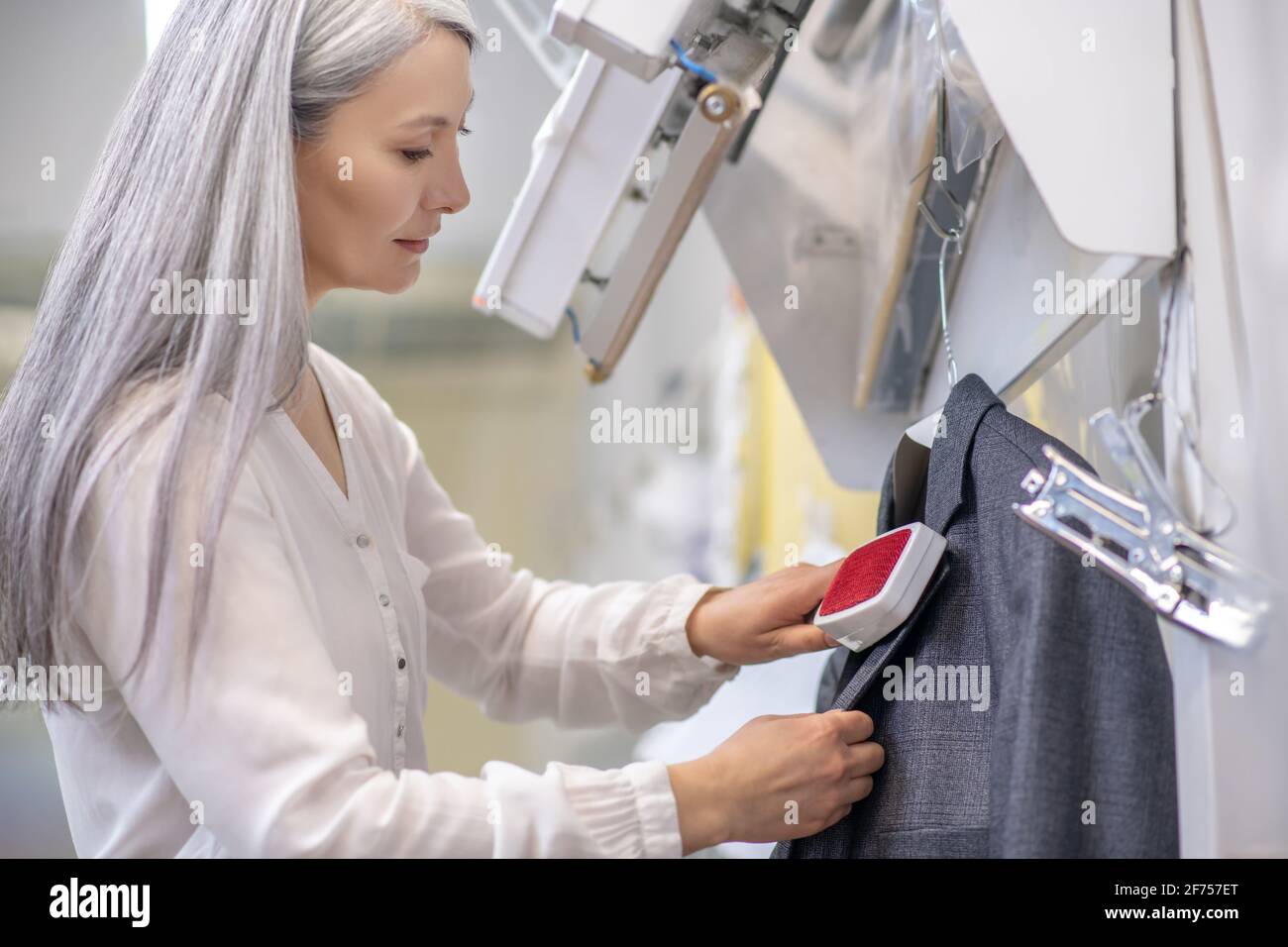 Attentive caring woman brushing hanging jacket Stock Photo