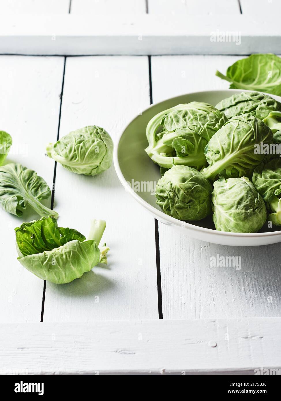 Fresh raw brussels sprouts in a bowl on a white wooden table. Stock Photo