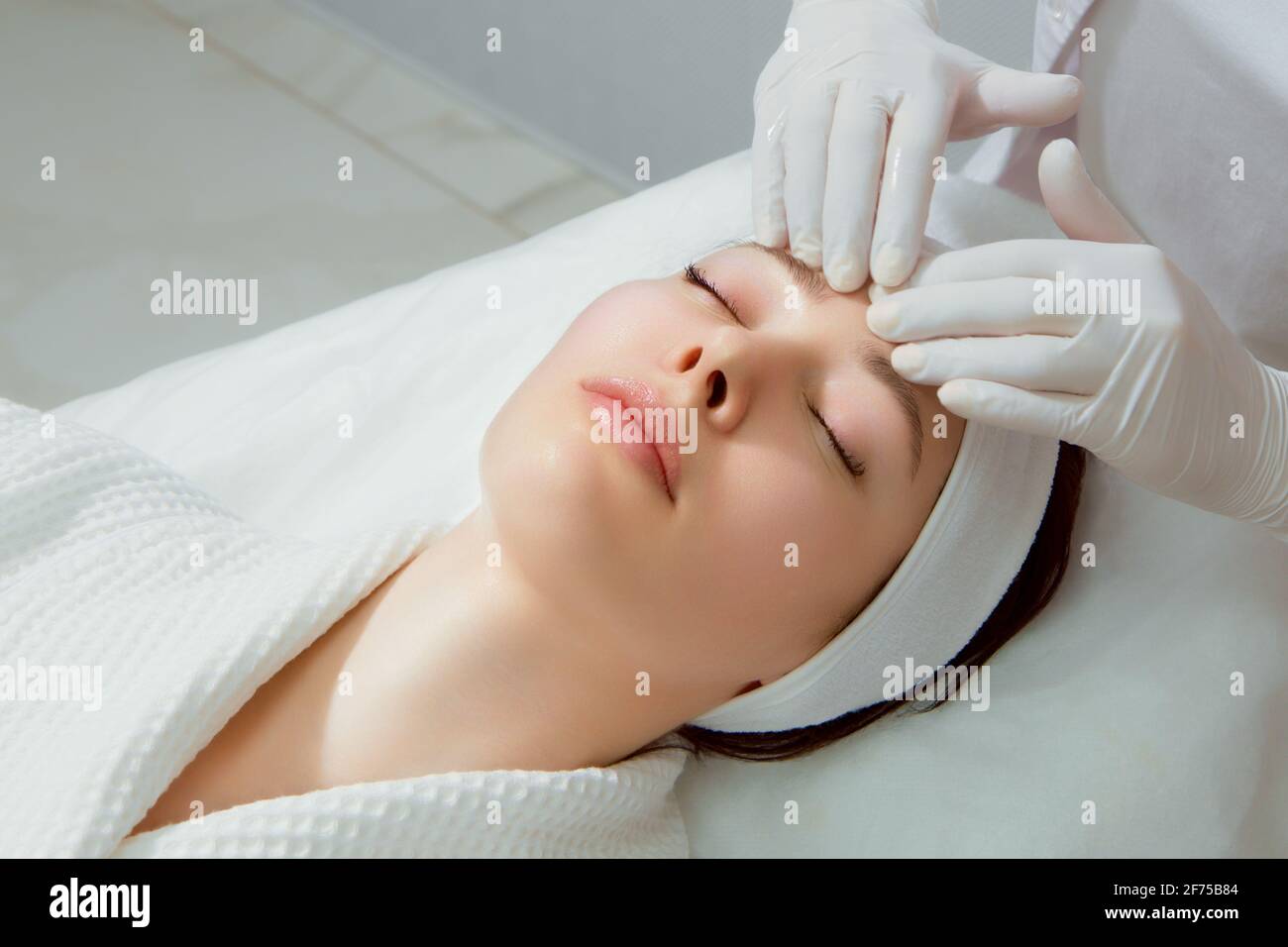 A young woman with perfect skin gets a facial massage at a cosmetology clinic Stock Photo