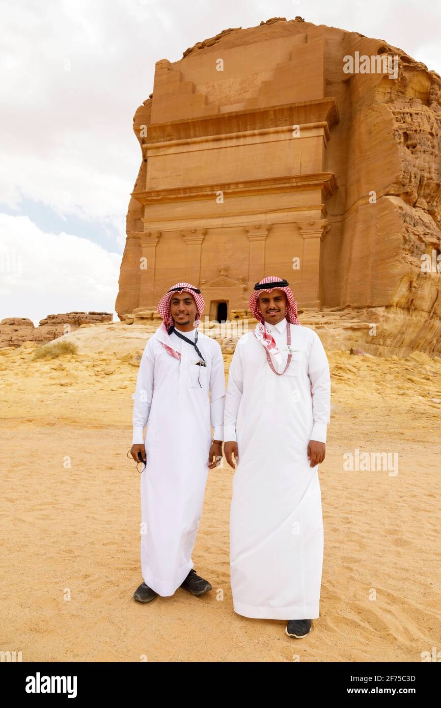 AlUla, Saudi Arabia, February 19 2020: Two young Saudi Arabian tour guides pose in front of the tomb of Lihyan son of Kuza, known as Qasr AlFarid, the Stock Photo