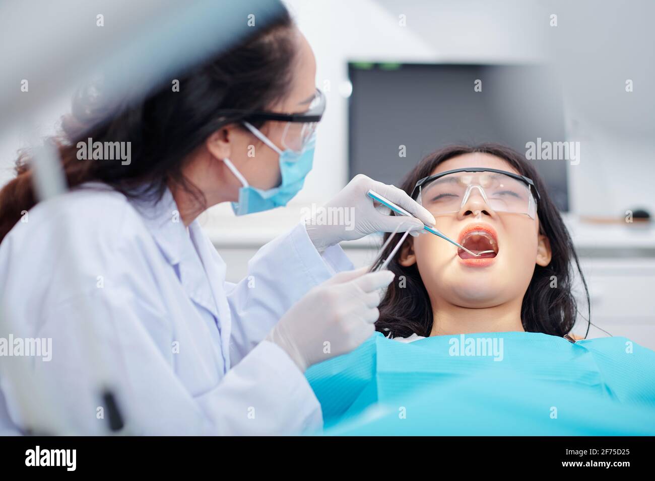Dentist using dental mirror and tweezers when checking teeth of young
