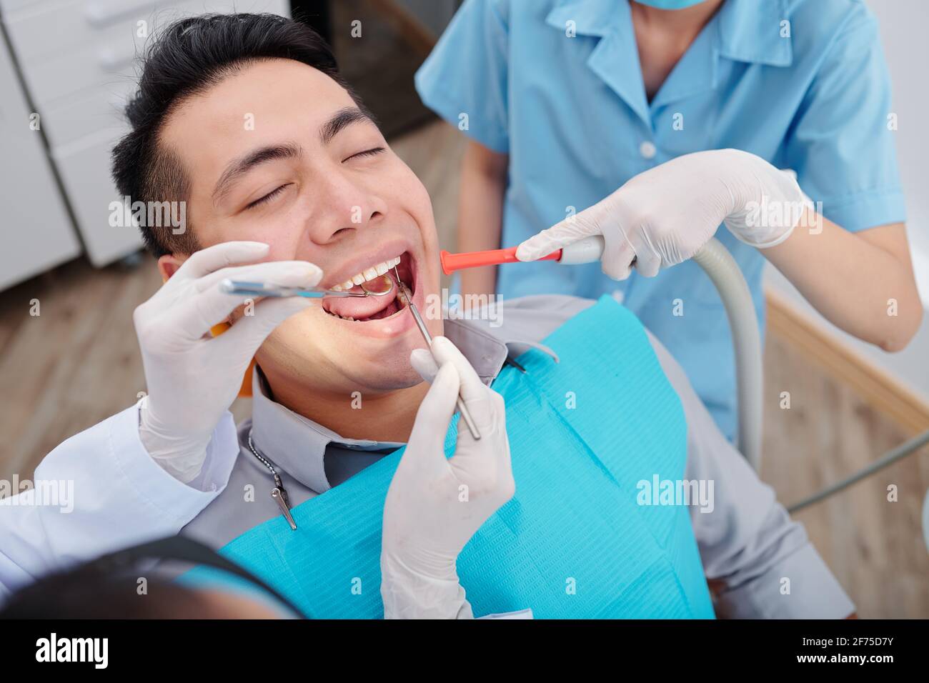 Dentist treating teeth of male patient when nurse putting saliva