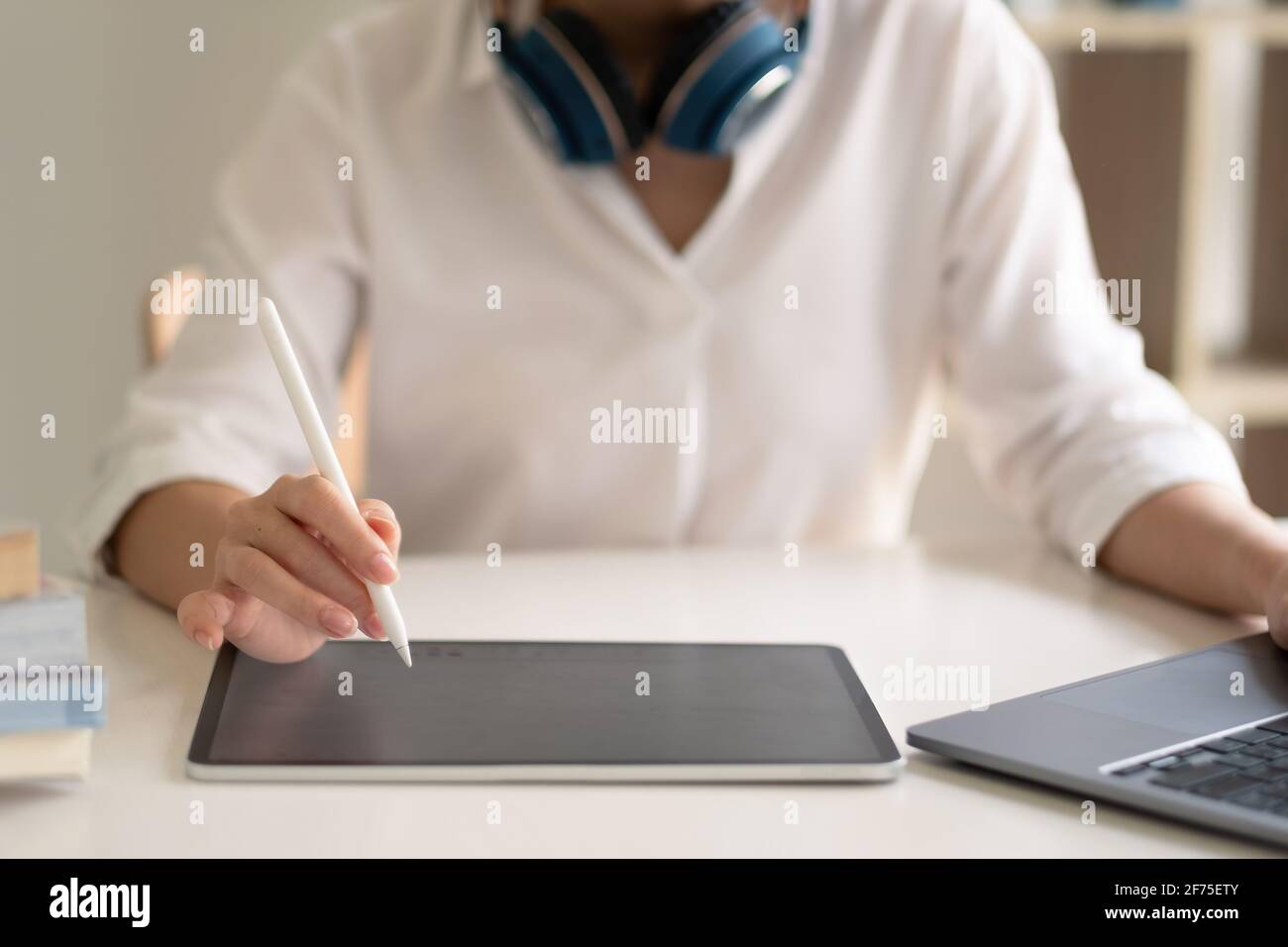 Close up of female worker working from home with digital tablet, laptop and headphone in home office room. Stock Photo