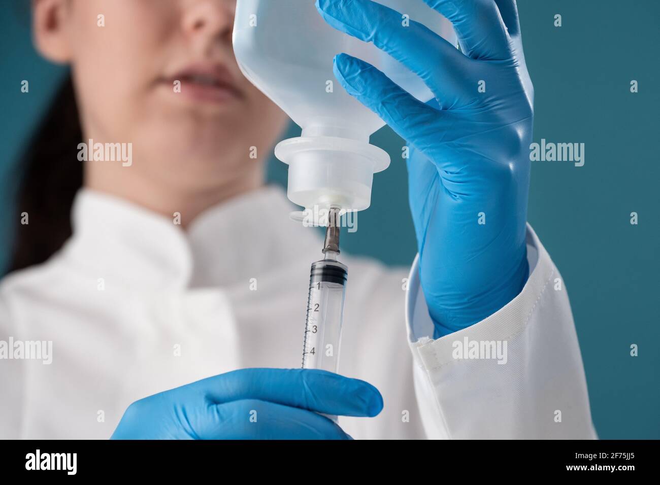 A young woman health worker draws a solution from a vial into a syringe for injection. Stock Photo