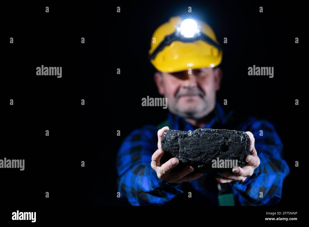 A miner holds a large lump of coal in his hands. A helmet with a lit flashlight on the miner's head Stock Photo