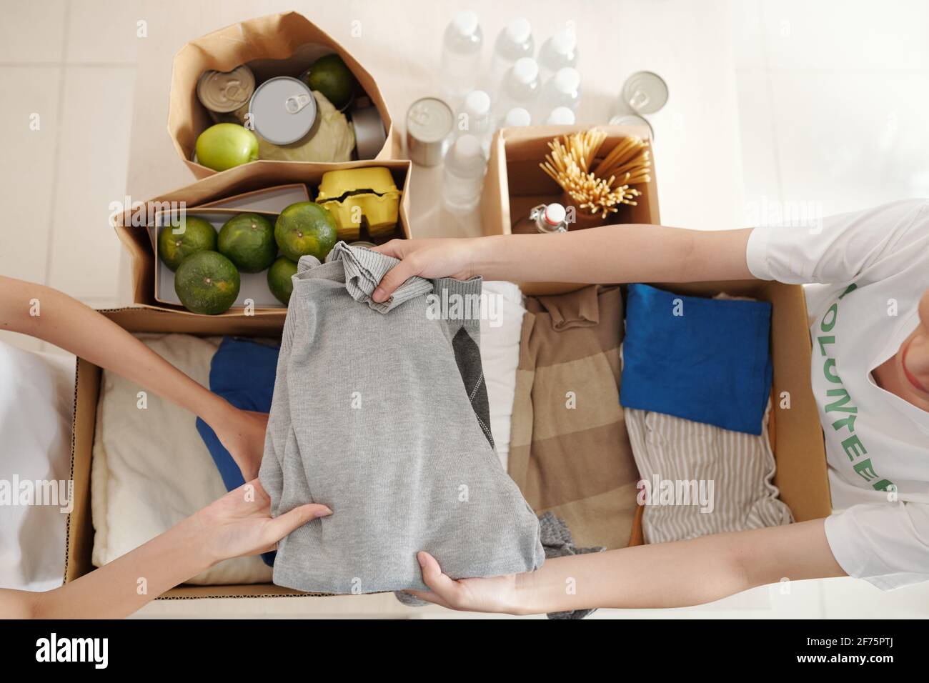 Hands of people packing fresh food and clean warm clothes in cardboard boxes Stock Photo