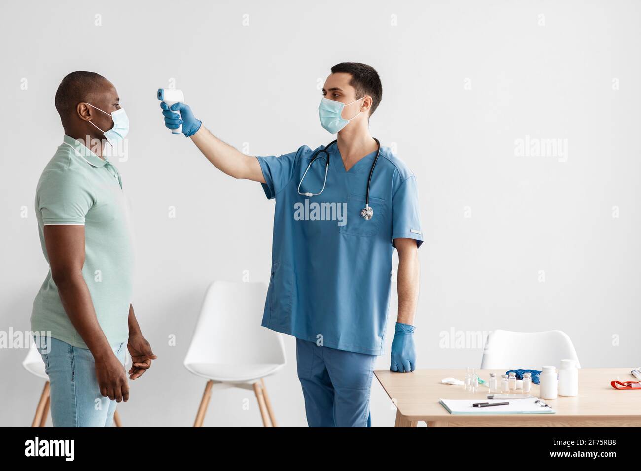 Measuring fever with gun, scanning forehead of african american man in clinic Stock Photo
