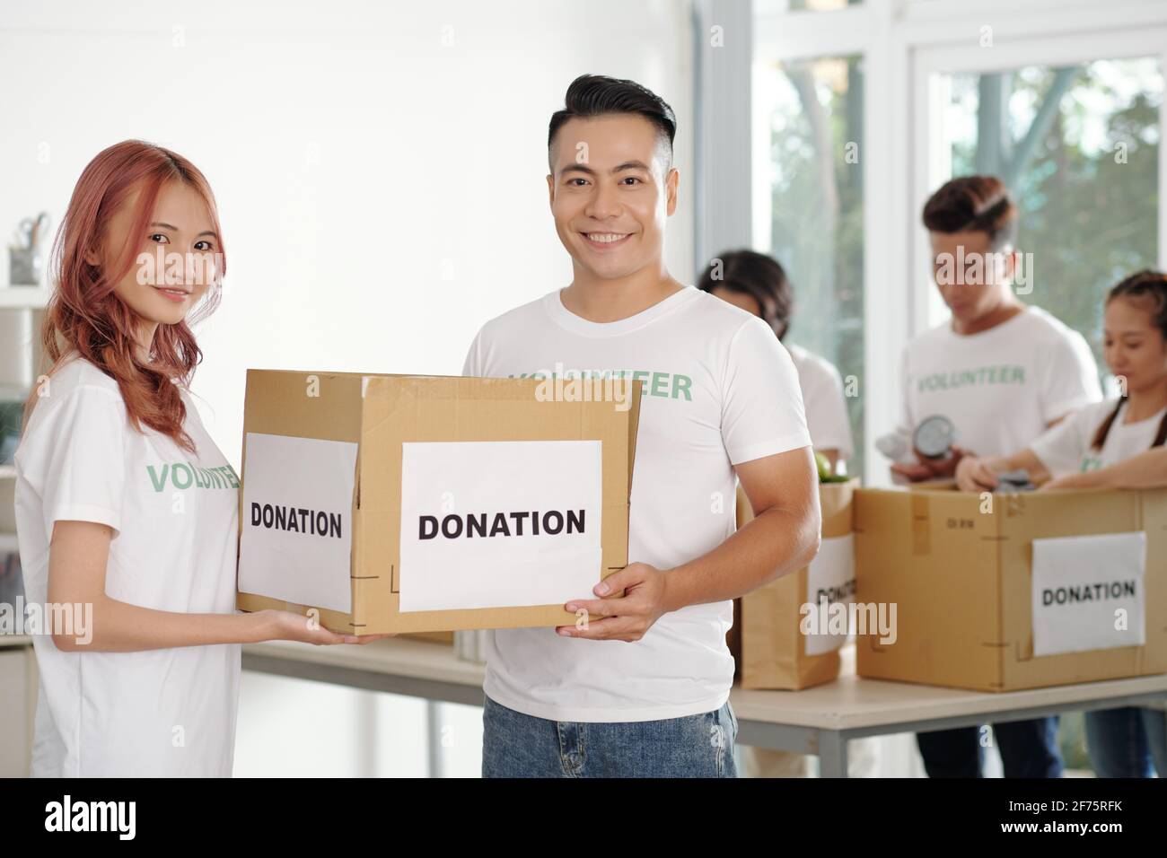 Young Asian couple working as volunteers in donation center, theay are packing boxed for people in need Stock Photo