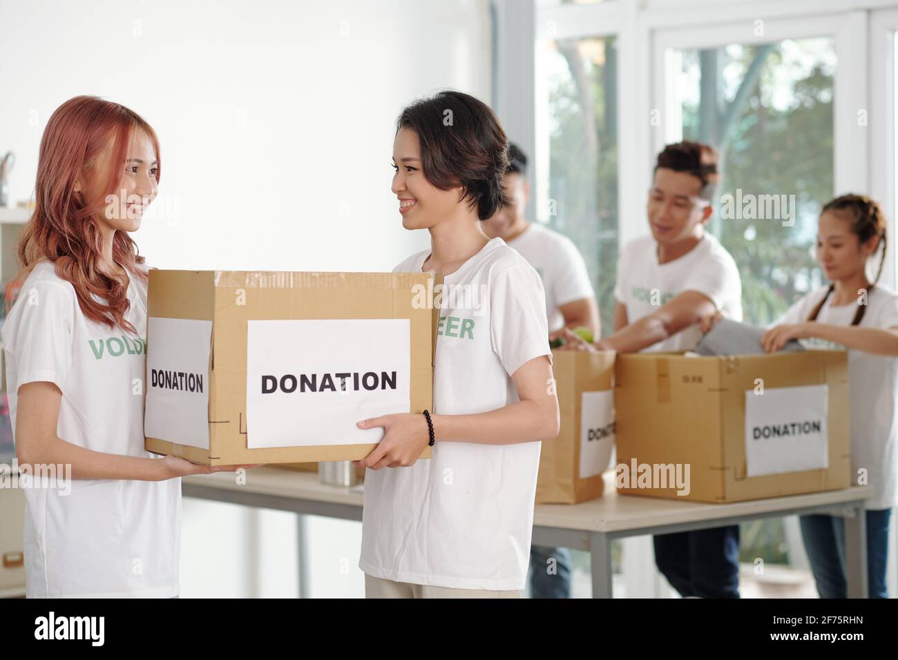 Young smiling female volunteers carrying big box of donated food or clothes Stock Photo