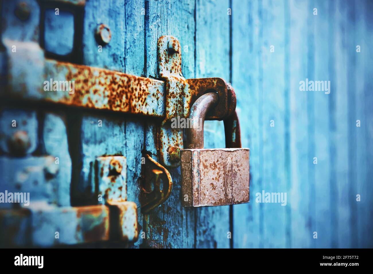 An old large lock hangs on a rust-covered blue abandoned wooden gate. Closed. Stock Photo