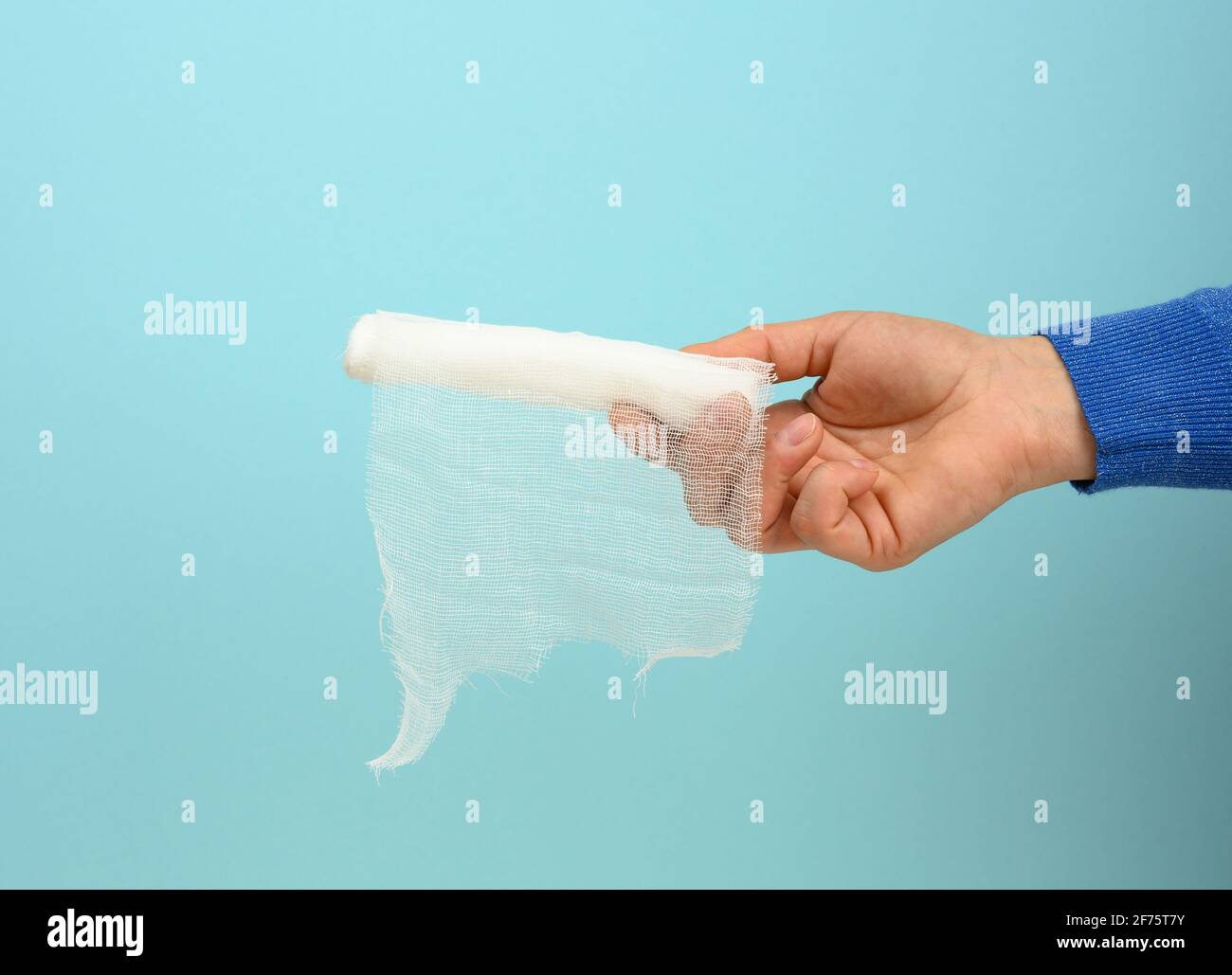 female hand holds white gauze bandage for bandaging limbs, blue background, close up Stock Photo