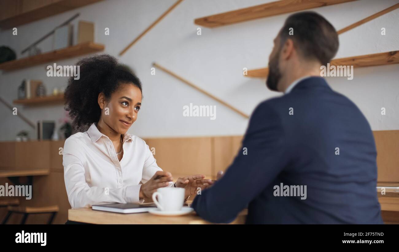 positive african american businesswoman talking with blurred partner during meeting in cafe Stock Photo